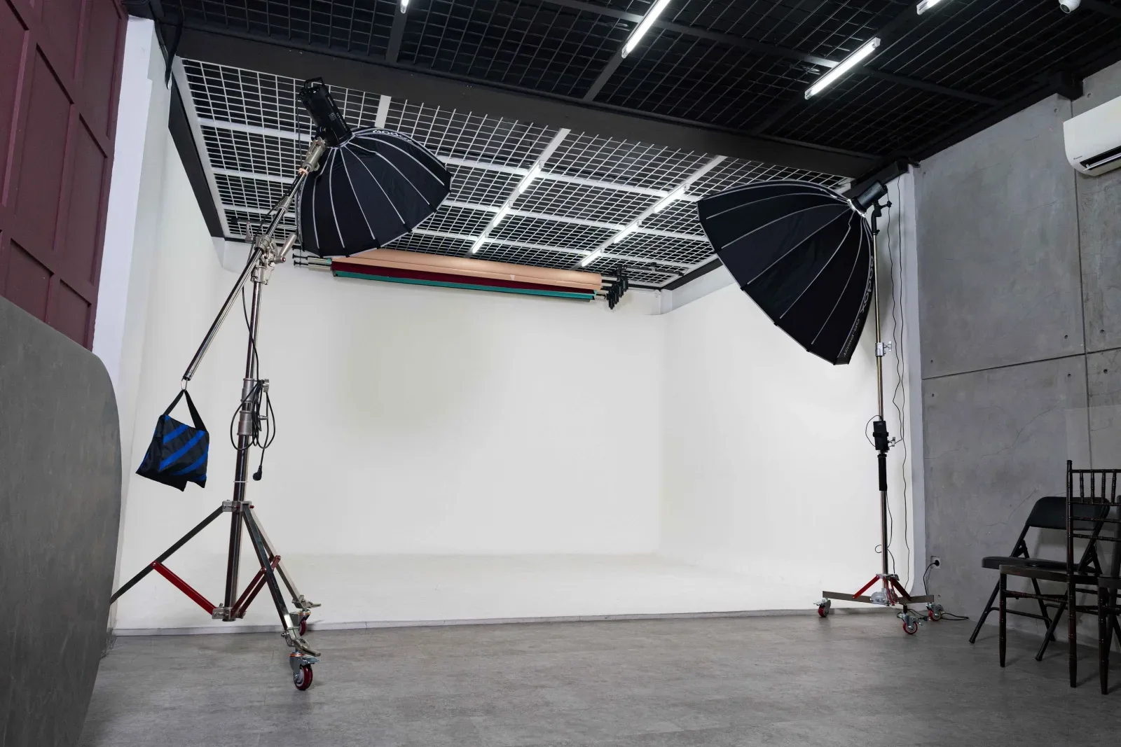 Ruang studio Limbo dengan cyclorama putih melengkung, dua octabox besar di C-stand beroda, dan tiga roll background tergantung di rel langit-langit.