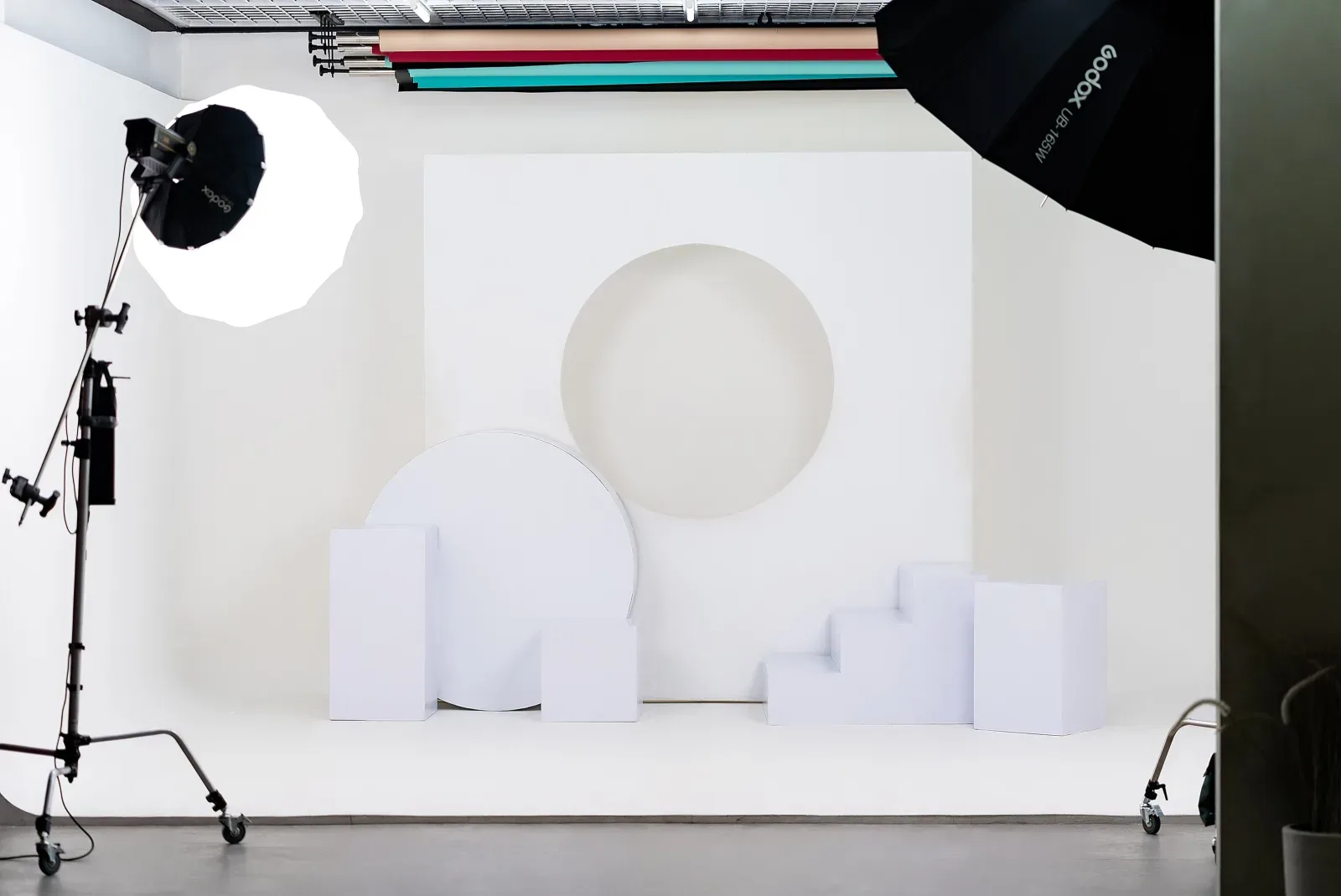 Cyclorama putih Limbo ditata dengan panel berlubang lingkaran, backdrop lengkung, dan blok podium putih, disorot softbox octa Godox.