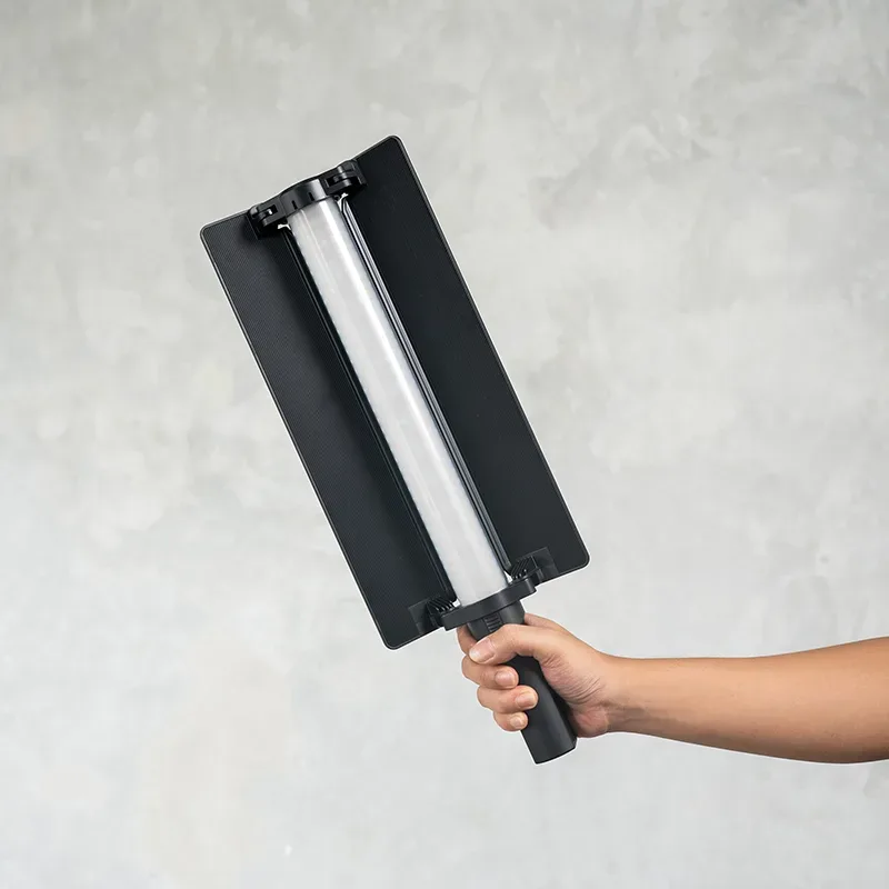 Lampu LED tabung RGB Godox LC500R Mini terpasang di bingkai panel hitam, dipegang tangan di depan dinding semen abu.