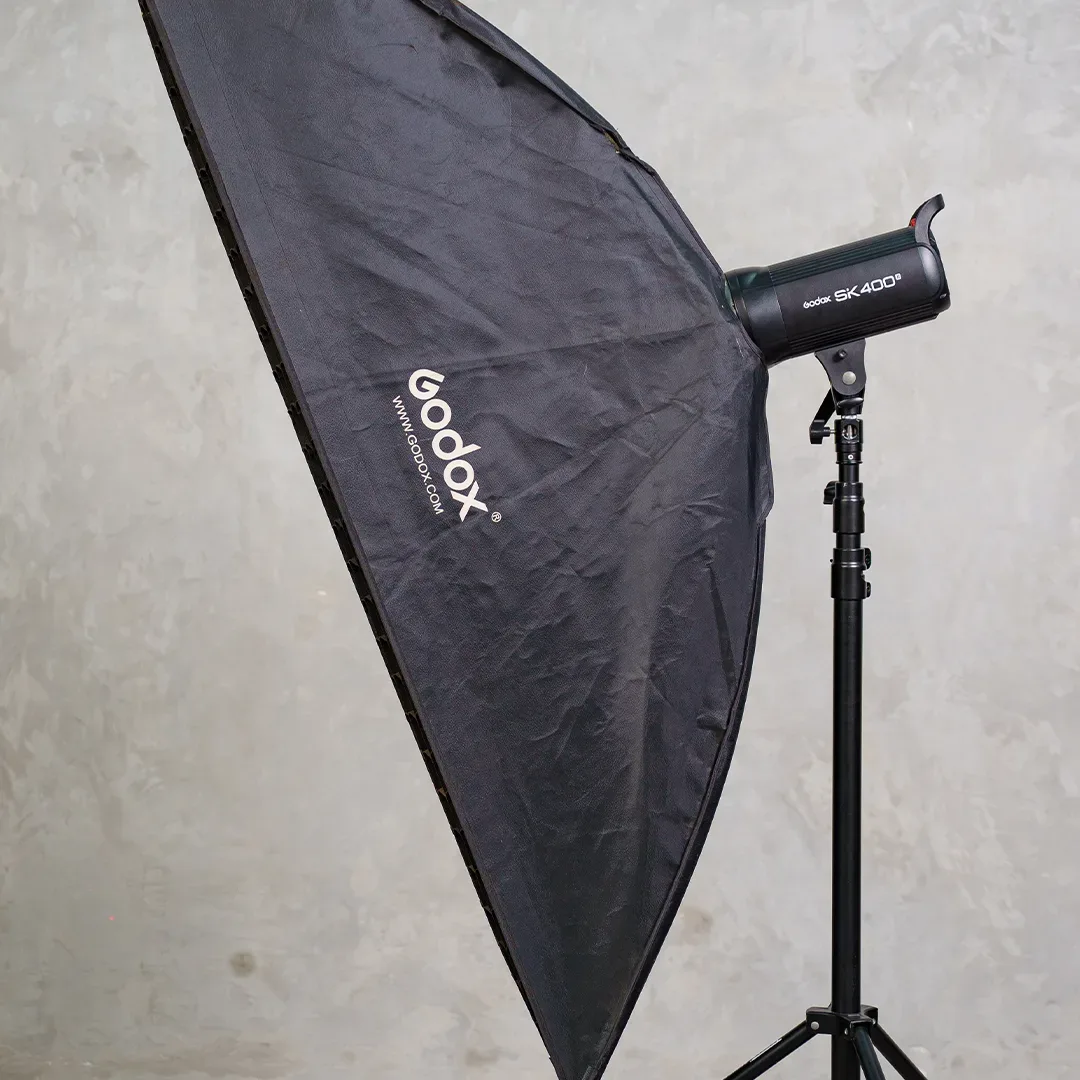 Lampu studio Godox SK400 II di light stand dengan softbox persegi panjang besar berlogo Godox, diambil dari samping.