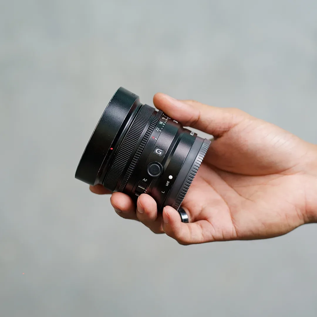 Lensa prime ringkas Sony seri G digenggam tangan; terlihat badge G, ring aperture, tombol focus hold, dan saklar AF/MF.