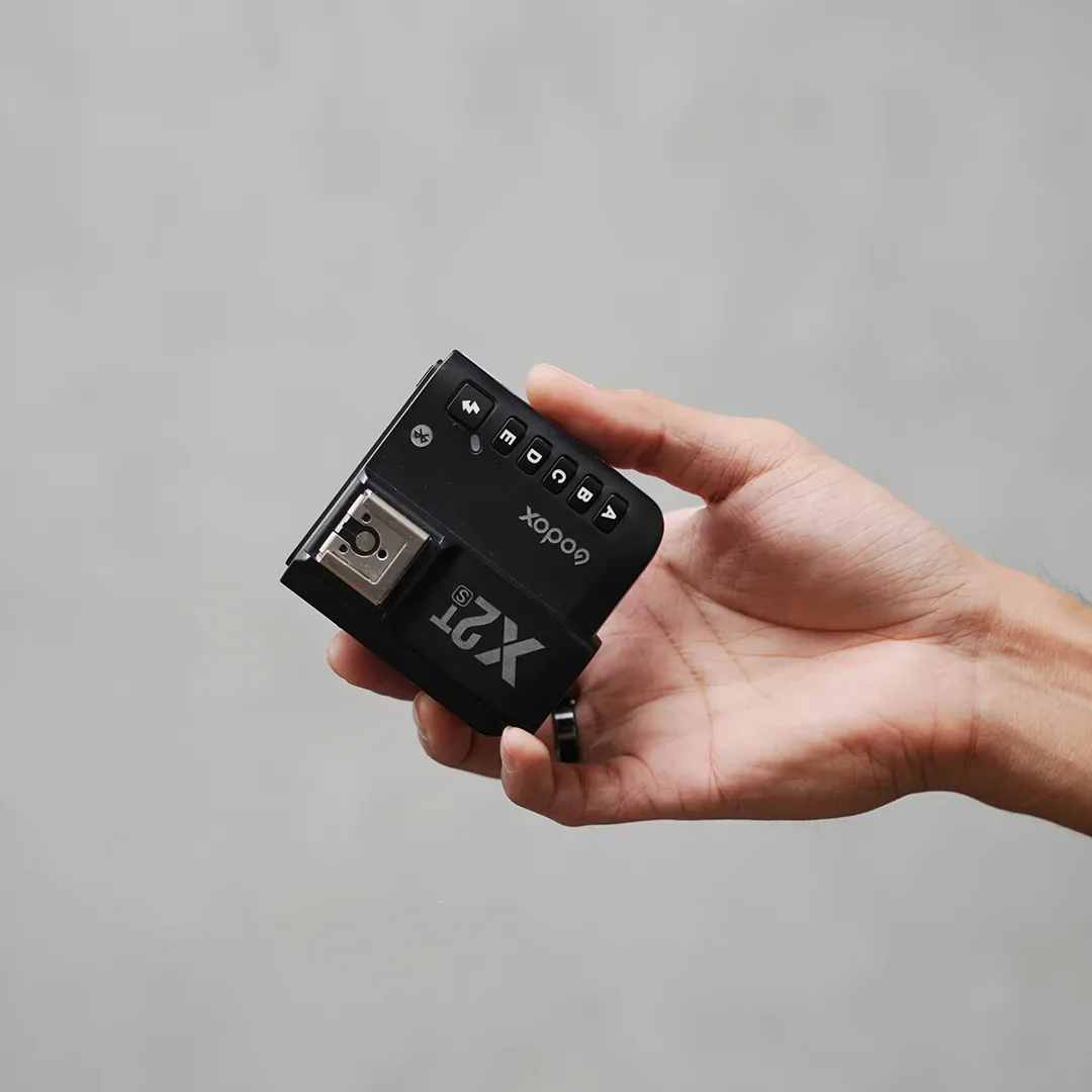 Trigger flash hitam Godox X2T untuk Sony digenggam telapak tangan; terlihat hot shoe, tombol grup A-E, dan tombol Bluetooth.
