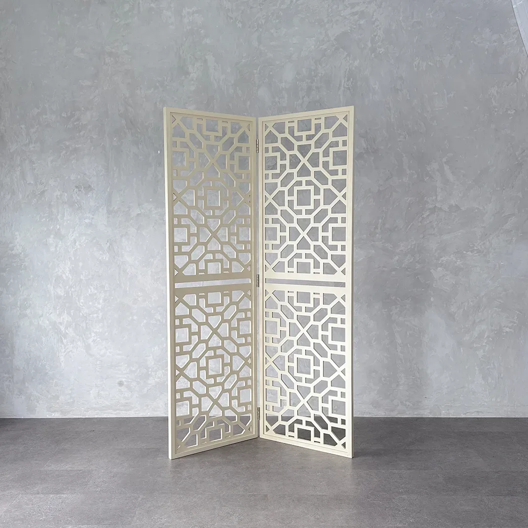 Sekat lipat dua panel dari kayu warna krem dengan ukiran geometris berlubang berdiri membentuk sudut di atas lantai beton.
