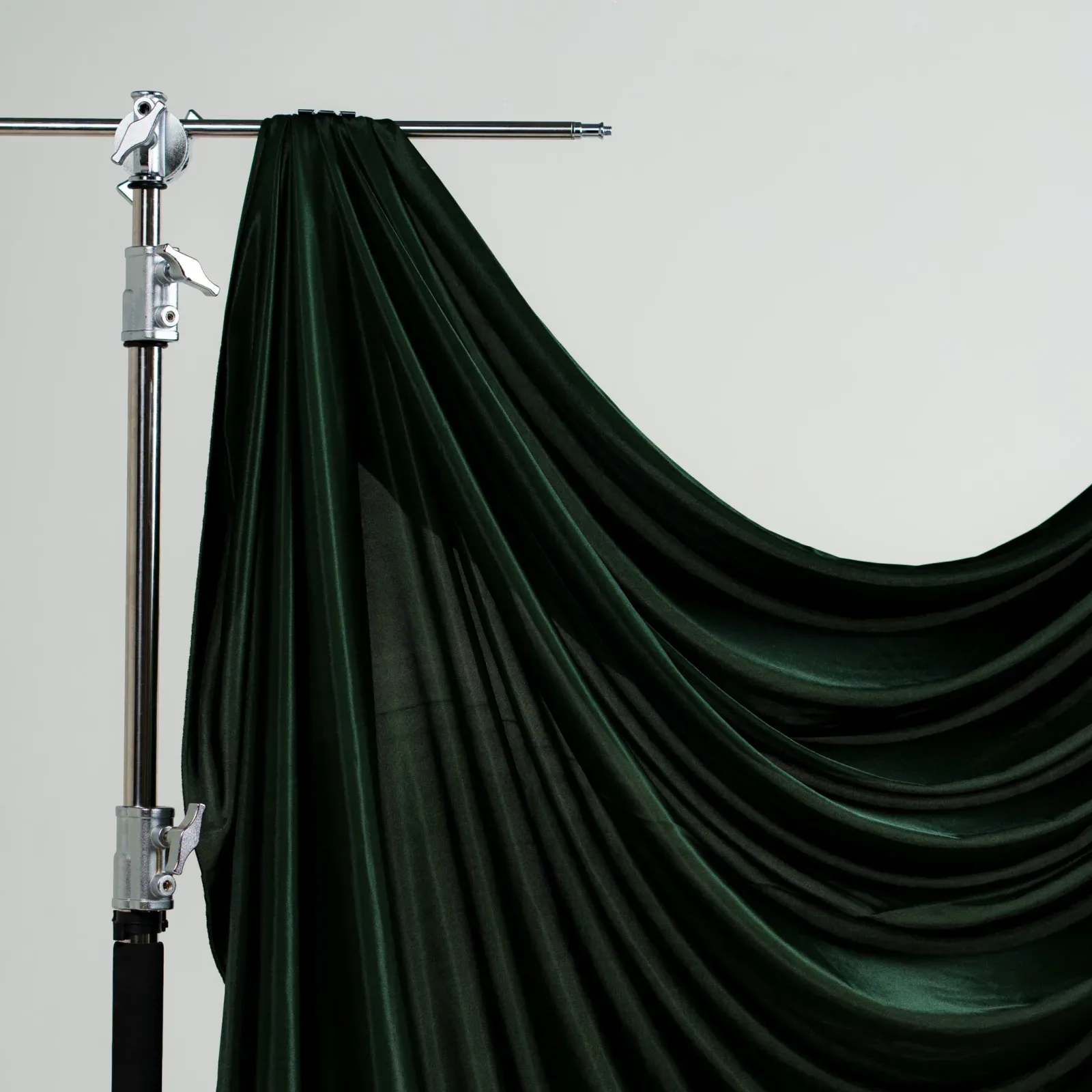 Kain latar hijau emerald gelap berkilau digantung di boom arm C-stand perak, jatuh melengkung membentuk drapery lebar.