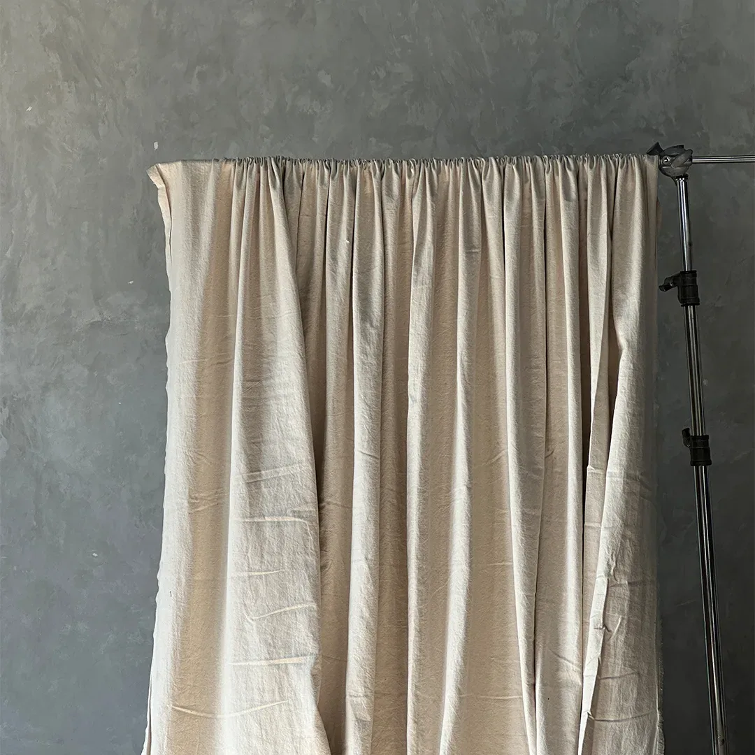 Kain latar krem natural bertekstur kanvas linen digantung pada batang di light stand dengan garis lipatan bekas simpan.